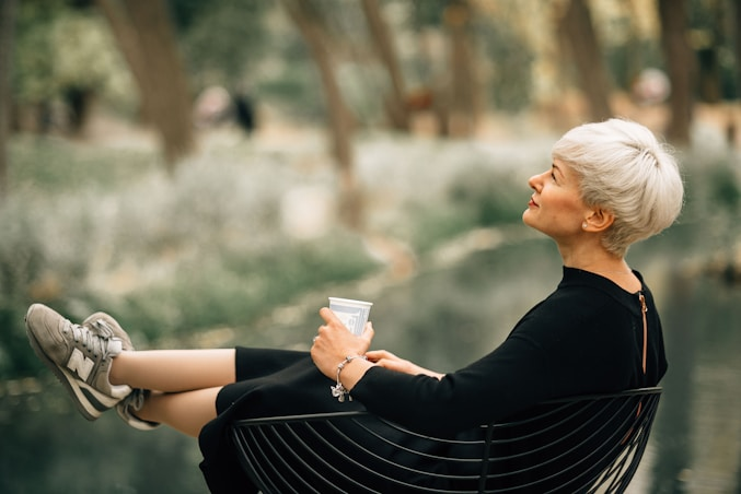 A lady peacefully sitting outdoors, holding a cup of coffee and enjoying the calm beauty of nature.