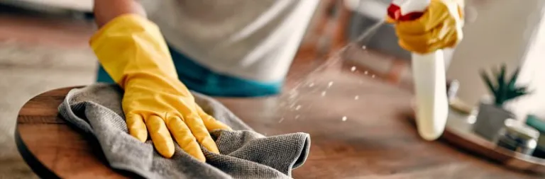 The hand of a man cleaning the surface of a table with a clothe and disinfectant