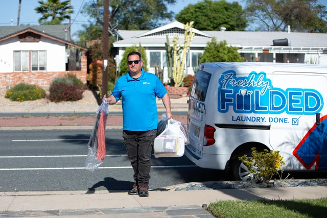 Freshly Folded team member carrying bagged laundry beside the branded company van