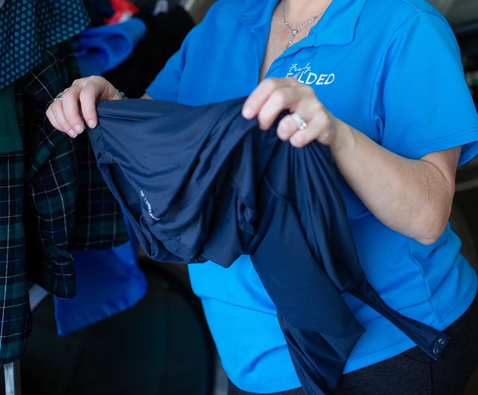 A Freshly Folded team member holding dark laundry beside a commercial dryer