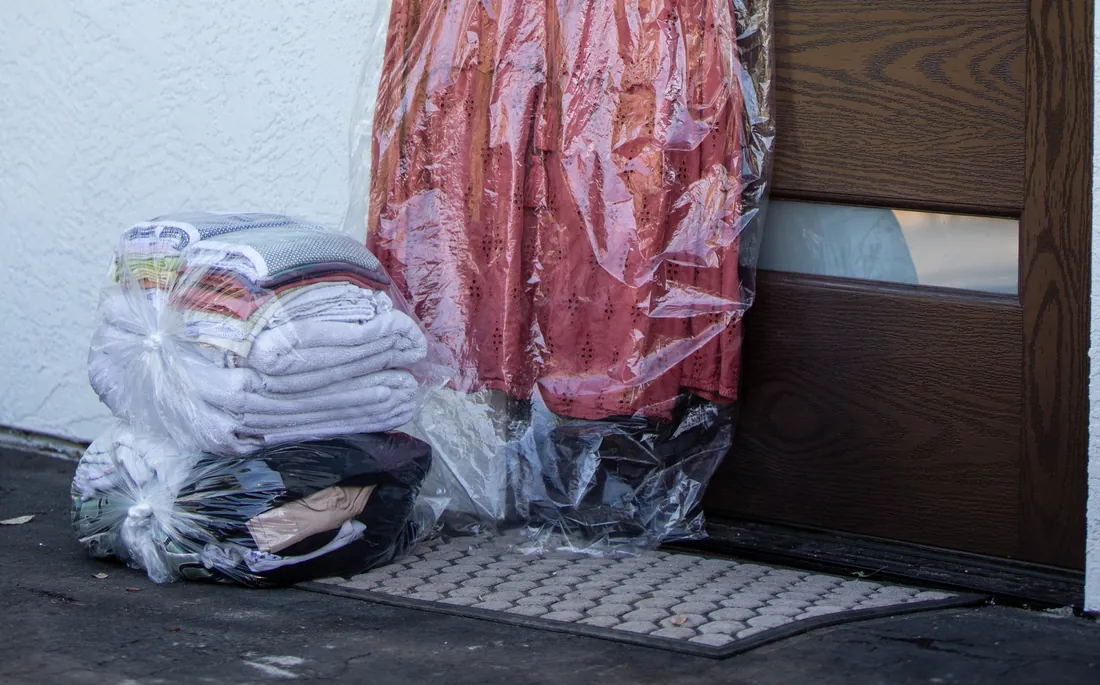 Clean folded towels, wrapped in plastic, waiting on a doormat beside a front door next to a bagged garment